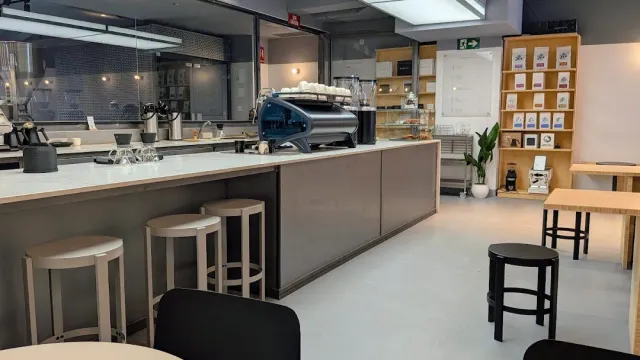דלפק לבן ארוך עם מכונת אספרסו כחולה, שרפרפים ומדף שקיות קפה