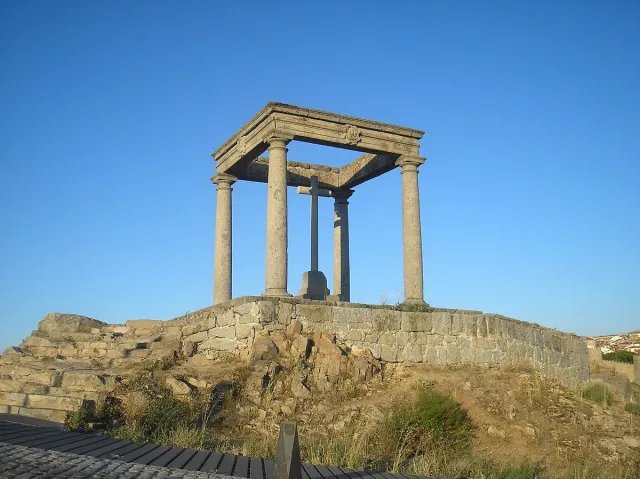 ארבעה עמודי אבן נושאים קורניז מרובע וצלב, על גבעה סלעית בשעת ערב
