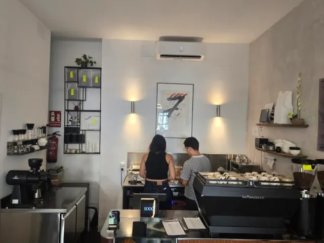 שני עובדים מאחורי דלפק צר עם מכונת אספרסו ומדפים על הקיר