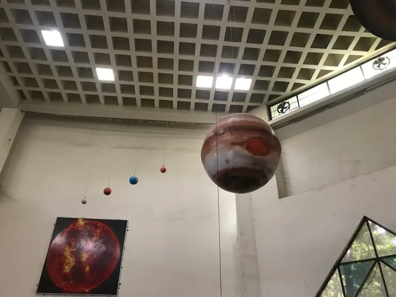 דגמי כוכבי לכת תלויים בחוטים מתקרת אולם מוזיאון, עם תמונת שמש על הקיר