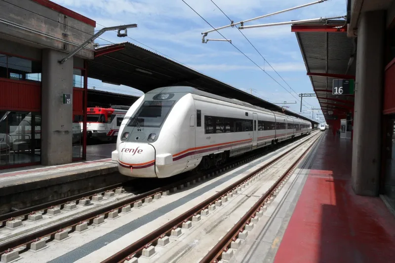 רכבת נוסעים לבנה של רנפה עומדת ברציף מקורה של תחנת רכבת, עם שילוט רציף 16
