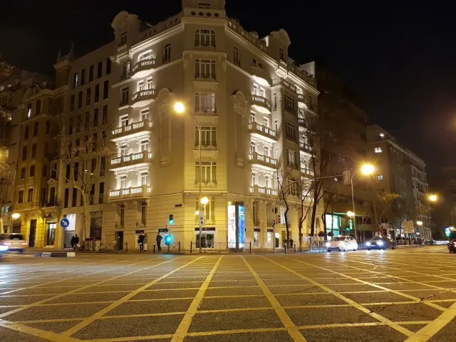 בניין פינתי מואר בלילה עם מרפסות, מול צומת רחב עם סימוני כביש צהובים