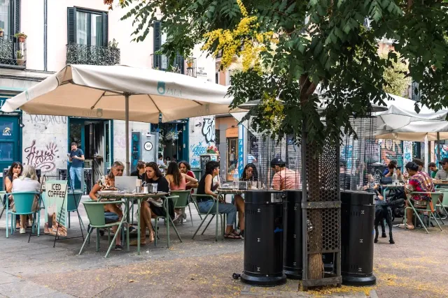 טרסת רחוב עם שמשיות וכיסאות ירוקים, וסועדים ליד שולחנות מתחת לעץ