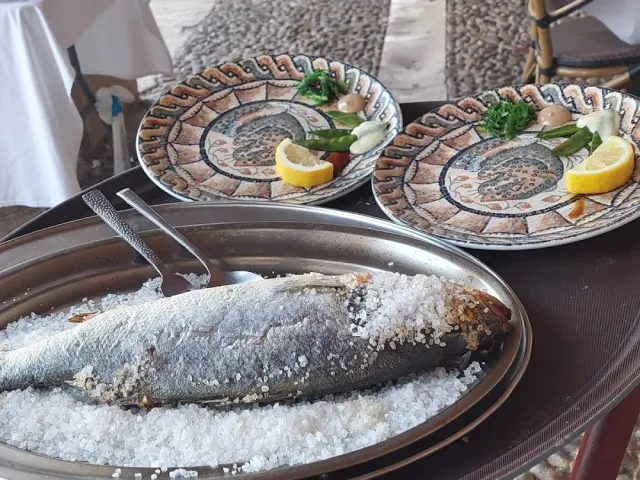 דג שלם אפוי במלח גס על מגש מתכת, ולצדו שתי צלחות מעוטרות עם לימון