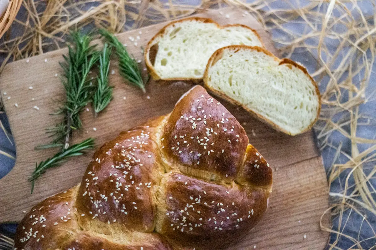 חלה קלועה עם שומשום פרוסה על קרש עץ, ארוחת שבת חמה במדריד